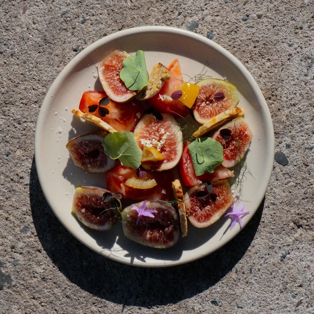 Ensalada de higos con jitomate y flores comestibles sobre piedra, un plato de temporada de Cosecha