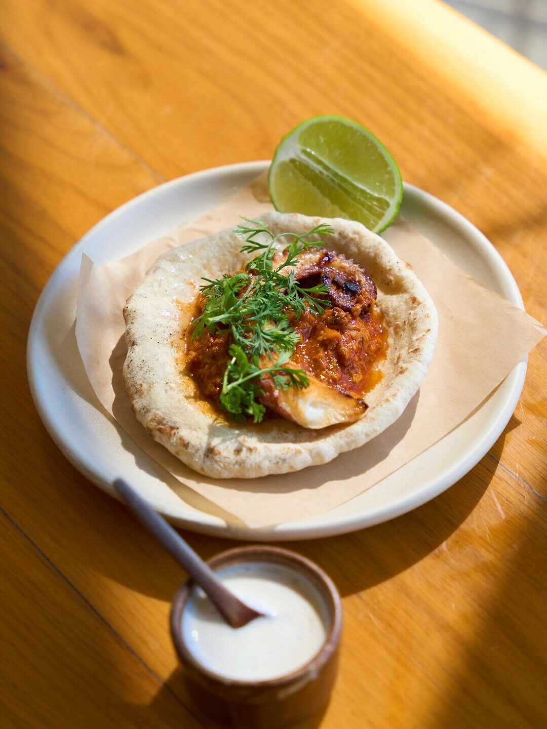 Pan pita con pulpo y chile, iluminado por luz natural sobre mesa de madera en Cosecha Taller de Cocina